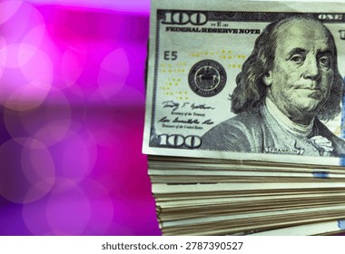 Thick stack of hundreddollar bills piled against neon pink backdrop, heavy bundle suggests bankroll or cash reserve, gritty texture contrasts with glamorous lighting of entertainment venue.
