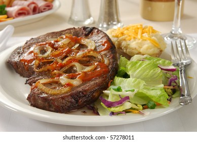 A Thick Steak Served With Sauteed Onions, Salad And Twice Baked Potato