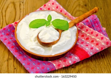 Thick Yogurt In A Clay Bowl, Basil, Spoon, Napkin Against A Wooden Board