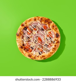 Thick-crust pizza with ham, mushrooms, and olives on a bright green background. Minimalist style, top view of pizza, junk food.