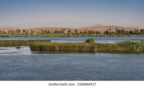 Thickets of green vegetation are visible on the shore and in the riverbed. Ripples on the blue water. Sand dunes against a clear sky. Copy space. Egypt. Nile - Shutterstock ID 2184864517