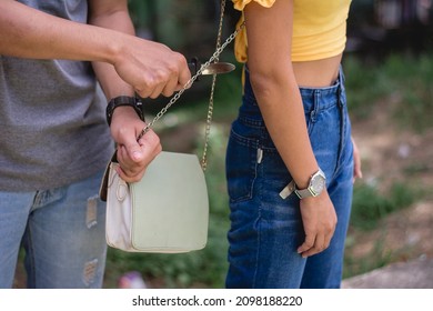 A Thief Attempts To Cut The Strap Of An Unaware Woman's Handbag. A Sneaky Theft In Progress In Broad Daylight.