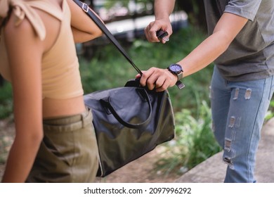 A thief attempts to quickly cut the strap of an woman's handbag. Trying to evade the criminal.