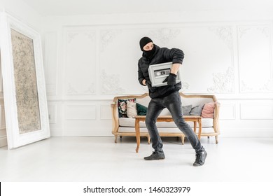 Thief with black balaclava stealing modern Electronic safe box. The burglar commits a crime in Luxury apartment with stucco.