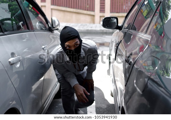 Thief in\
black balaclava trying to break into\
car