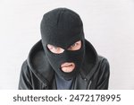 A thief in a black jacket. A man in a black balaclava with an evil expression on his face. An aggressive bandit on a white background. The concept of crime or theft.