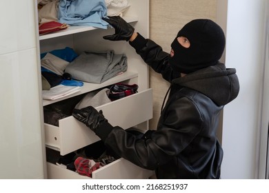 A thief in a black mask searches a closet with clothes in search of cash or valuables. Apartment theft. A search of the house. Petty crime