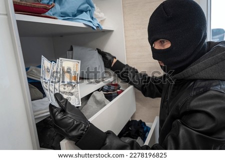A thief in a black mask searches a closet with clothes in search of cash or valuables. Apartment theft. A search of the house. Petty crime