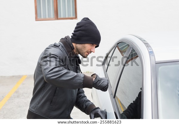 Thief\
breaking into car with fist in broad\
daylight