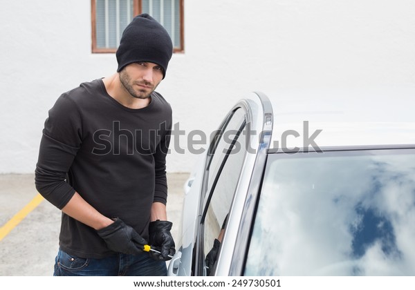 Thief breaking into car with screwdriver in
broad daylight