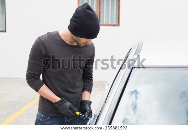 Thief breaking into car with screwdriver in\
broad daylight