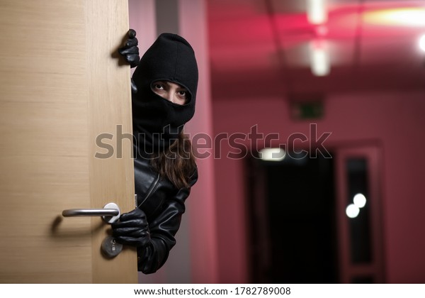 Thief\
broke into the apartment. House robbery by woman in a black jacket\
and black mask holding black gun. Burglar in a mask. Thief in a\
mask trying to break into other people\'s\
house