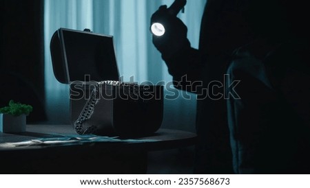 A thief commits a burglary, stealing valuables in a dark apartment. A jewelry box illuminated by a beam from a lantern in the hands of a criminal close up. Crime, robbery, property security concept.