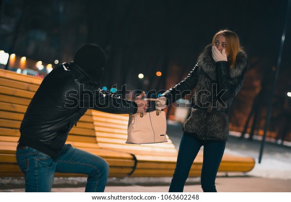 Thief Dangerous man or masked robber with knife\
attacking shoulder bag. Robber or thief holding knife burglarize to\
steal the money wallet in woman\'s bag, while sitting at restaurant\
and don\'t careful