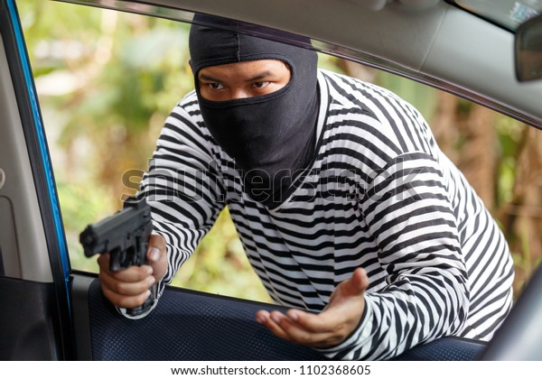 Thief Dangerous man or masked robber with weapon\
attacking shoulder bag. Robber or thief holding gun to steal the\
money wallet and smart phone in woman\'s bag, while sitting in car\
and don\'t careful.