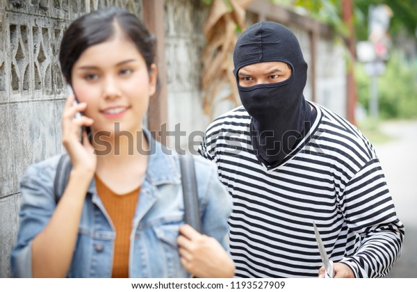 Thief Dangerous man or masked robber with knife\
attacking shoulder bag. Robber or thief holding knife burglarize to\
steal the money wallet in woman\'s bag while standing near her car\
and don\'t careful.