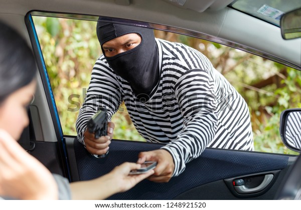 Thief Dangerous man or masked robber with weapon\
attacking shoulder bag. Robber or thief holding gun to steal the\
money wallet and smart phone in woman\'s bag, while sitting in car\
and don\'t careful.