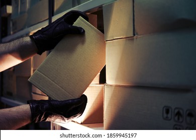 Thief hands with gloves steal a box of goods in a warehouse in the dark. Concept of problems with theft of goods and postal parcels