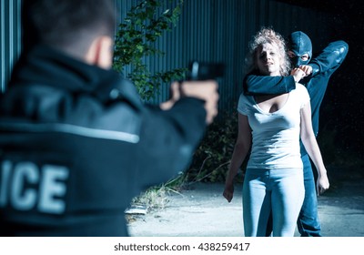 Thief Holding A Woman Hostage While A Policeman Is Pointing Gun At Him