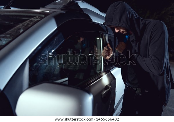 thief\
intruding car with flashlight and crowbar at\
night