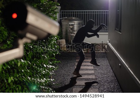 Thief jump down from wall break into a house at window being caught by CCTV, surveillance camera