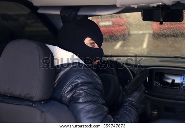 Thief in mask with gun\
sitting in car