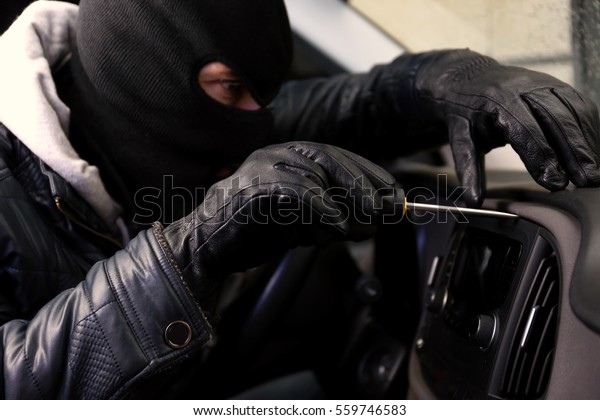 Thief\
in mask trying to steal car radio with\
screwdriver