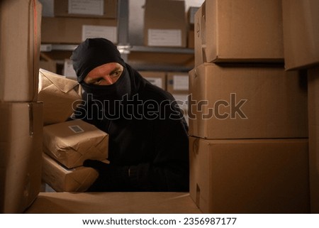 A thief stealing boxes in a warehouse at night in the dark. Warehouse and store security concept. Copy space