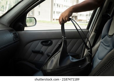 Thief steals a handbag from the passenger seat from an open window car. View from inside the automobile interior. Concept of robbery.