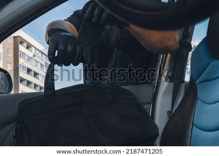 Thief steals a smartphone from a bag from the passenger seat from an open car window. View from inside the automobile interior. Concept of robbery.
