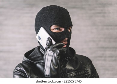 The thief is talking on the phone in a black mask. The extortionist demands money for the kidnapping. a phone fraudster commits a crime, violates the law. concept of telephone fraud. - Shutterstock ID 2215293745