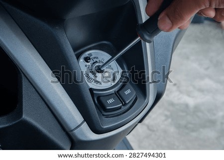 thief using a screwdriver tool to break into a motorcycle ignition lock, representing vehicle theft and security vulnerabilities. Ideal for news crime prevention campaigns, insurance agency websites