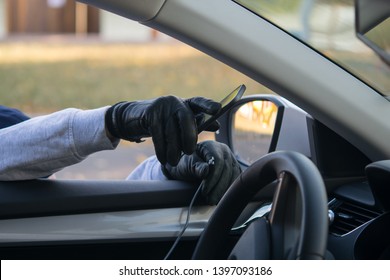 The Thief's Hand In A Black Glove, Takes The Smartphone From The Front Of The Car, Through The Open Glass, Breaking The Wire