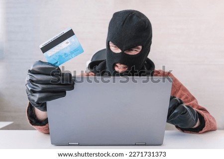 Thieves hold credit cards using a laptop computer for password hacking activities. Cyber crime concepts. a male thief holds a credit card in his hand and picks up a password to steal money