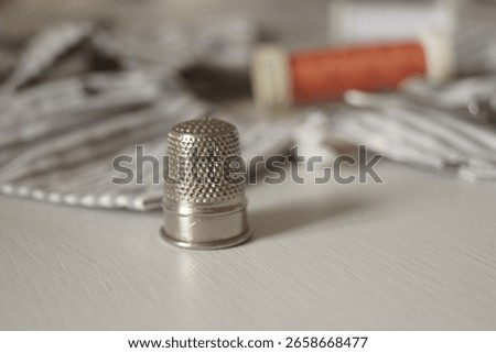 A thimble, scissors and an orange spool of thread spread near a handmade grey vintage collar on a white background