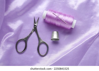 Thimble, scissors and sewing thread on purple cloth, flat lay. Space for text