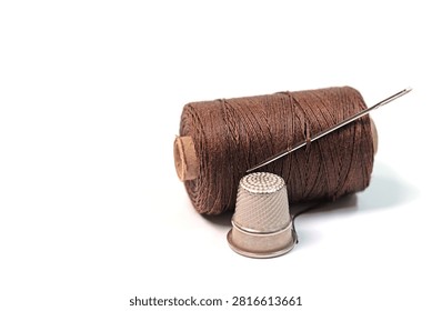 Thimble, sewing needle, and thread against a white background
