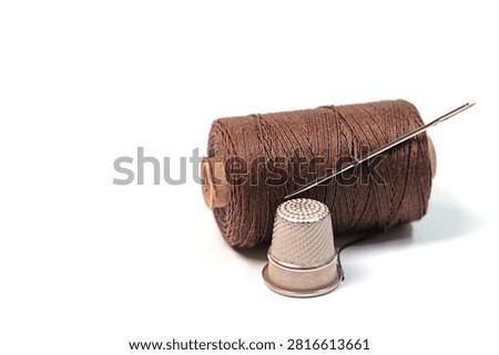 Thimble, sewing needle, and thread against a white background
