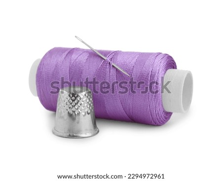 Thimble and spool of violet sewing thread with needle isolated on white