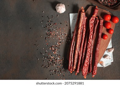 Thin appetizing spicy smoked sausages with herbs, tomatoes, spices and garlic on a dark background. Copy space