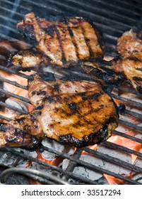 Thin Center Cut Bone In Pork Chops Cooking On A Charcoal Barbecue Grill With Grill Marks And Hot Coal Flames