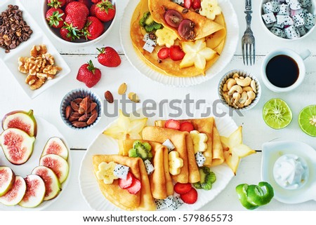 Thin crepes with carambola, pitaya, strawberry, kiwi, banana, figs, lime and honey over white table. Top view of healthy breakfast over white background.