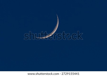 Thin crescent moon against a deep blue twilight sky. Minimalist night scene with copy space, calm atmosphere, astronomy and space concept, natural celestial background.