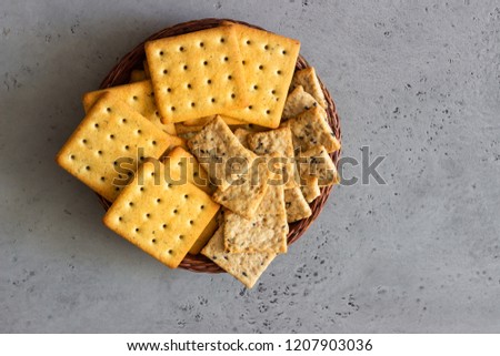Thin crispy salted crackers with seeds and herbs on grey concrete background. 