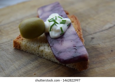 Thin Cut Of Port Wine Derby Cheese On A Crispy Slice Of Bread With Two Green Olives And A Dollop Of Sauce 