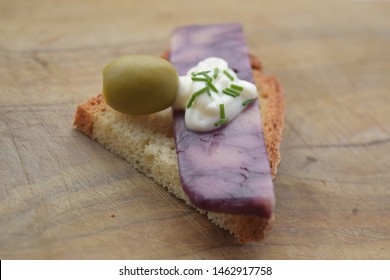 Thin Cut Of Port Wine Derby Cheese On A Crispy Slice Of Bread With Two Green Olives And A Dollop Of Sauce 