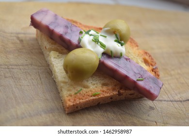 Thin Cut Of Port Wine Derby Cheese On A Crispy Slice Of Bread With Two Green Olives And A Dollop Of Sauce 