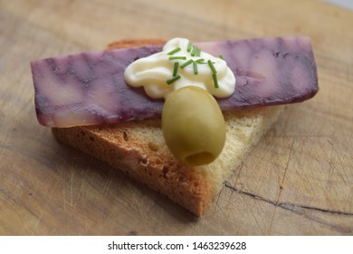 Thin Cut Of Port Wine Derby Cheese On A Crispy Slice Of Bread With Two Green Olives And A Dollop Of Sauce 