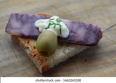 Thin Cut Of Port Wine Derby Cheese On A Crispy Slice Of Bread With Two Green Olives And A Dollop Of Sauce 