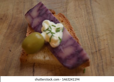 Thin Cut Of Port Wine Derby Cheese On A Crispy Slice Of Bread With Two Green Olives And A Dollop Of Sauce 